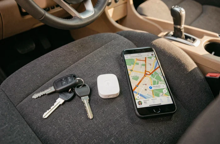Balise Bluetooth, clés de voiture et smartphone avec application GPS posés sur un siège auto