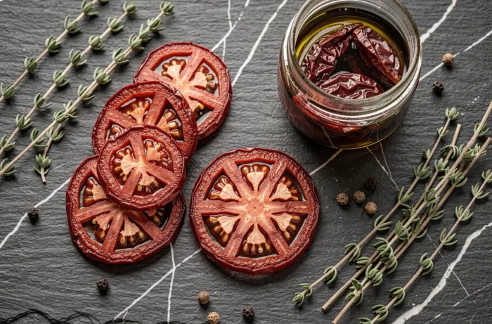 Vue du dessus de tomates séchées au déshydrateur disposées sur une ardoise avec un bocal d'huile d'olive et des herbes séchées